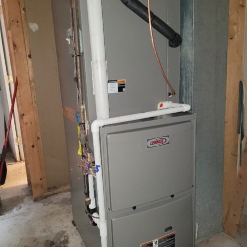 A Lennox HVAC unit installed in a utility room, surrounded by unfinished wooden framing. Visible pipes, wiring, and ductwork are connected to the unit, which stands on a concrete floor.