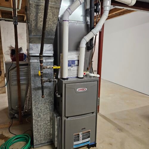 A Lennox furnace with attached ductwork and PVC pipes is installed in a basement with unfinished walls and concrete flooring. A green garden hose is coiled on the floor nearby.